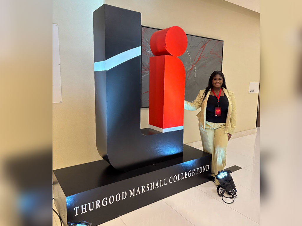 A Florida A&M University representative poses beside the Thurgood Marshall College Fund display during a 2026 TMCF event, highlighting the organization's commitment to supporting students attending historically Black colleges and universities. Photo courtesy of Faith Paul.