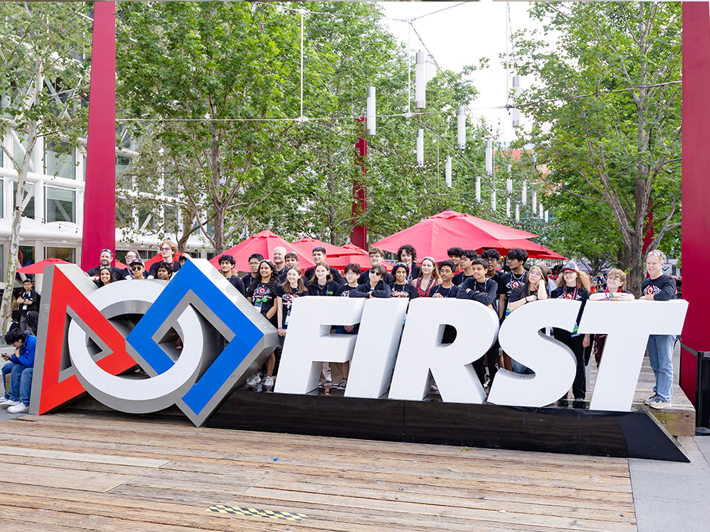 High school students standing in front of the FIRST sign