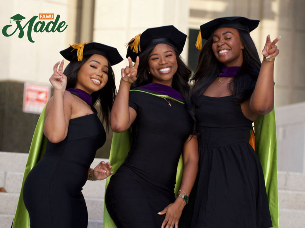 Three College of Law graduates in regalia doing the rattler strike.