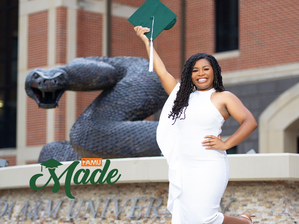Makenzie Harris in a white cocktail dress standing in front of the giant rattler with her commencement cap in hand