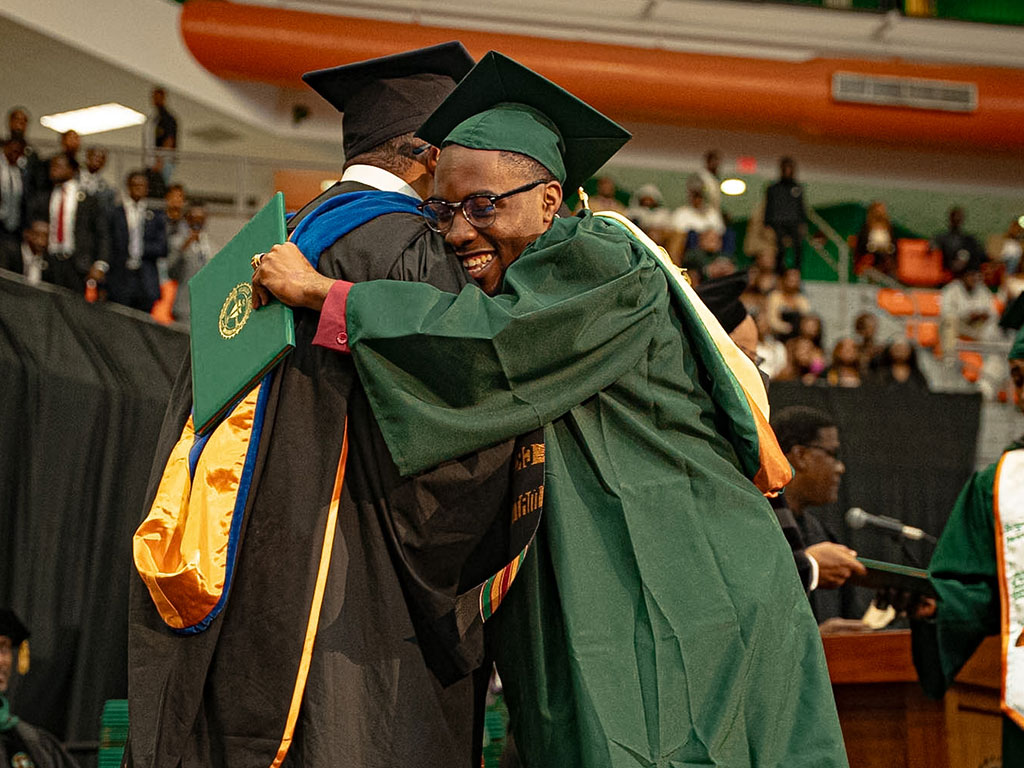 A male graduate hugging an administrator.