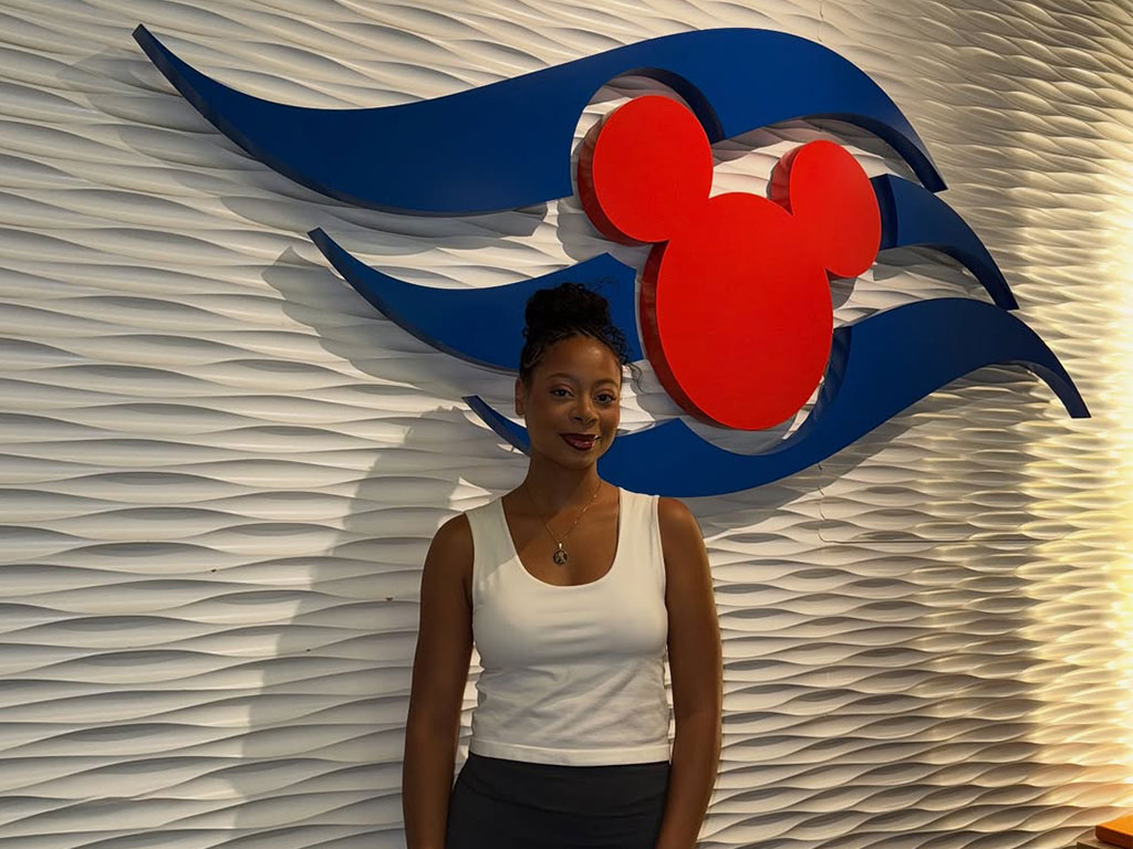 Florida A&M University alumna Rae’Kwan Bostic poses in front of the Disney Cruise Line emblem, where she brings the character of Princess Tiana to life as part of her growing career in entertainment.