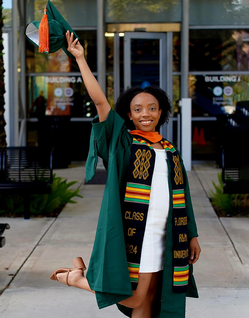 Briona Carswell, adorned in her green cap and gown, poses outside.